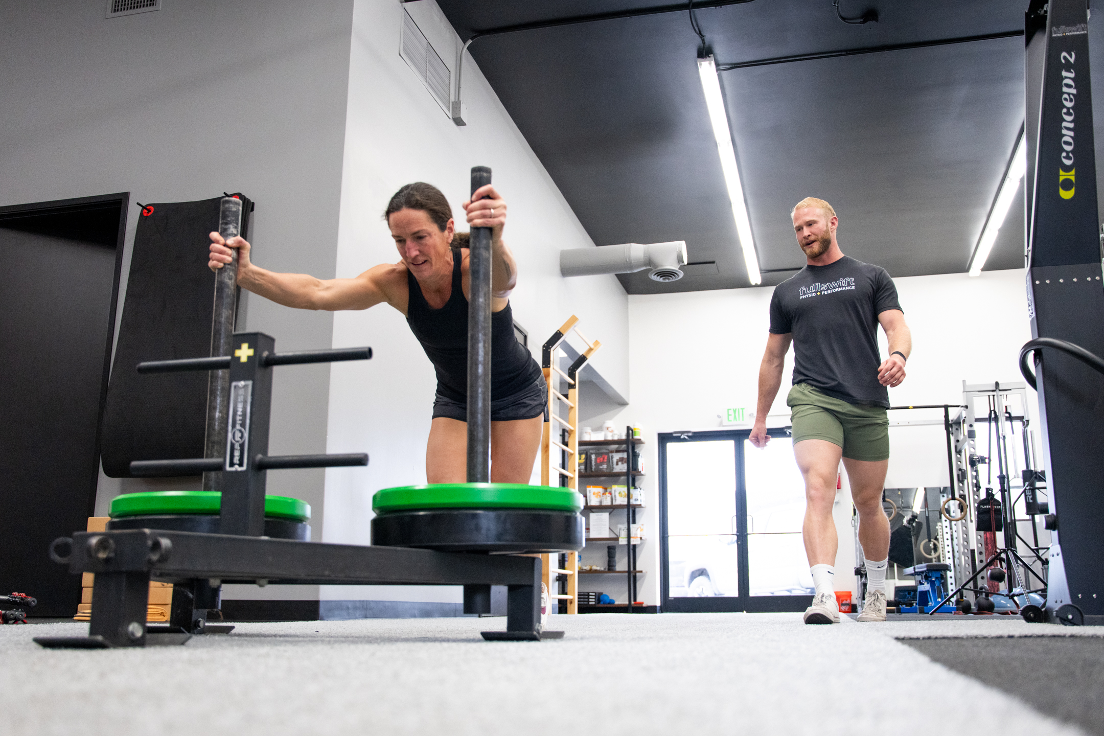 Physical therapist guiding an athlete through a strength and conditioning exercise in a performance gym setting